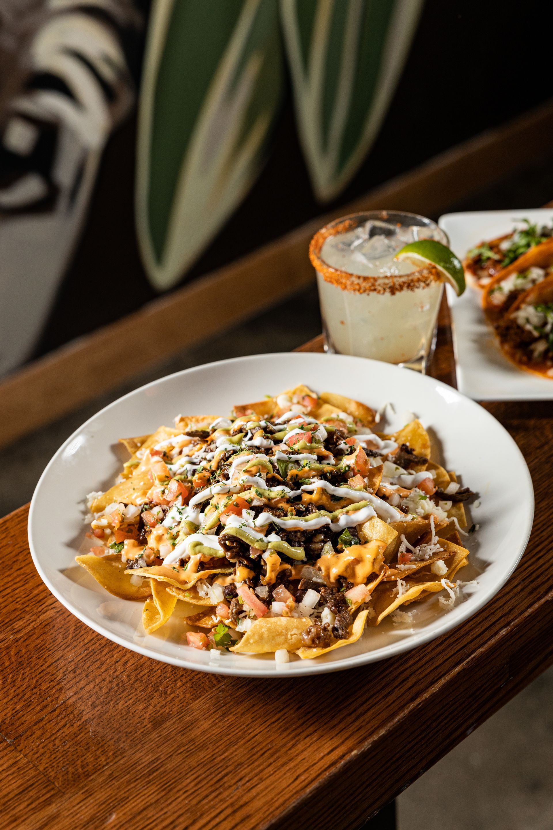A plate of nachos and a margarita on a wooden table at Con Safos in downtown Denver CO, with a view of Coors Field.