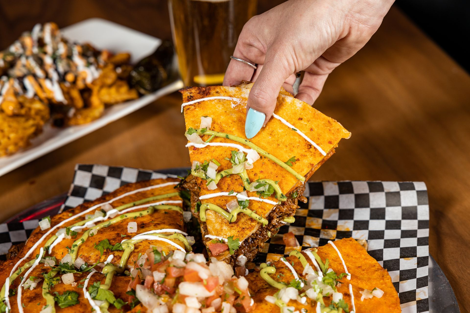 A person is taking a slice of quesadilla from a plate of food at Con Safos in downtown Denver CO, with a view of Coors Field.