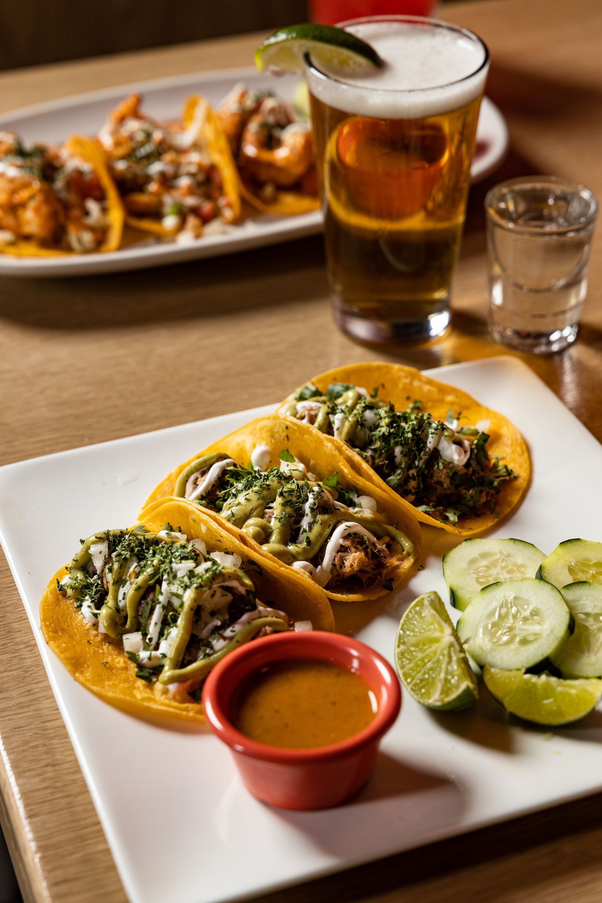 A plate of tacos and a glass of beer on a table at Con Safos in downtown Denver CO, with a view of Coors Field.
