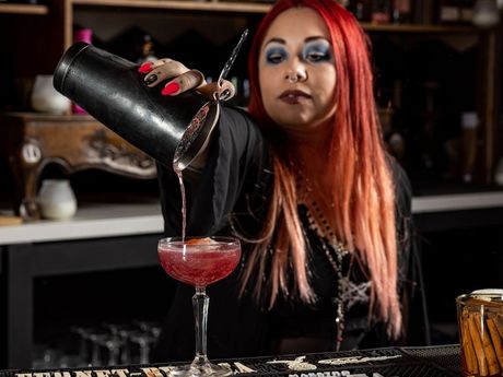 A woman is pouring a drink from a shaker into a glass.