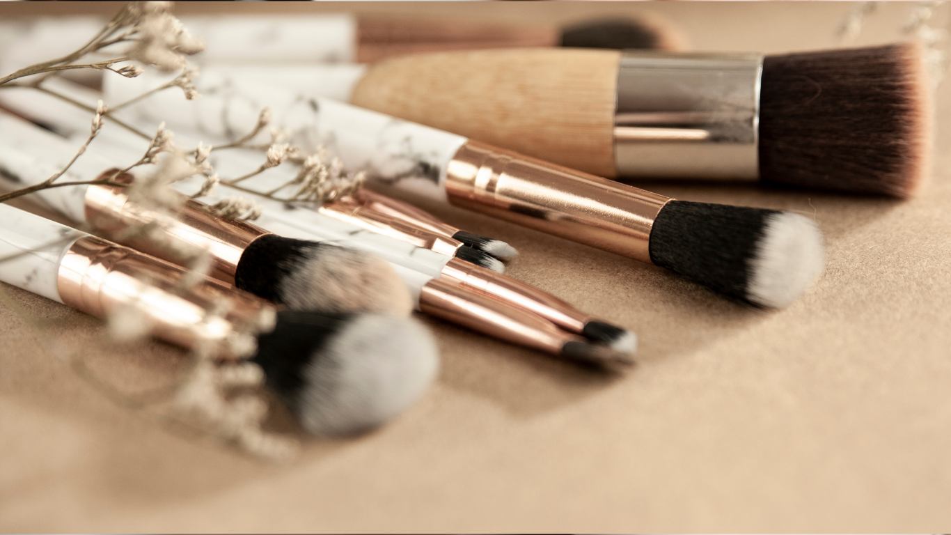 Assorted makeup brushes with rose-gold handles on a beige surface, some with soft bristles.
