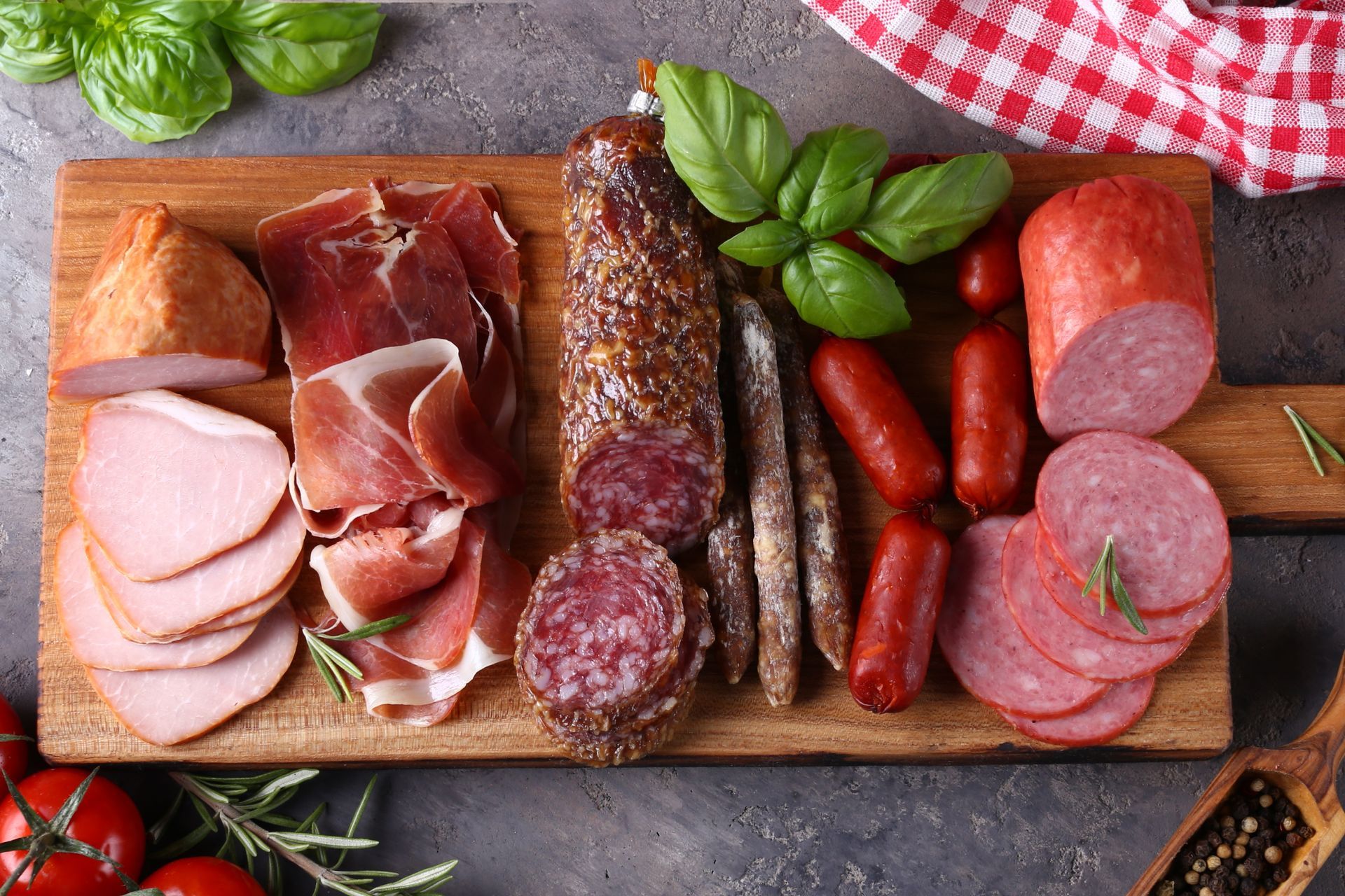 Charcuterie board with various cured meats, herbs, and tomatoes.