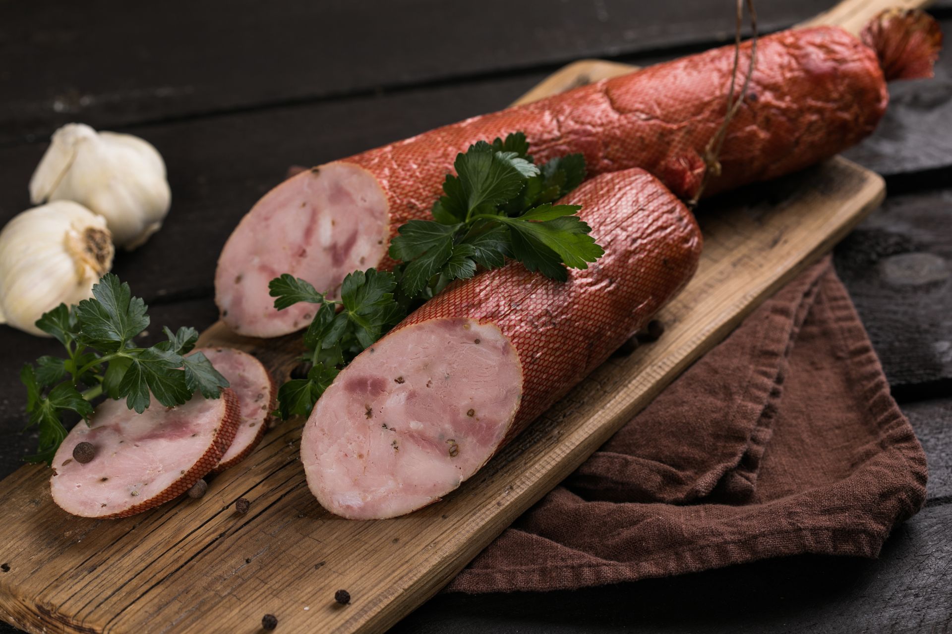 Sliced sausage on wooden board, with garlic and parsley.