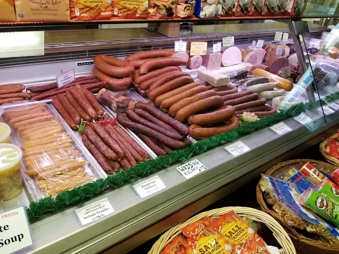 Deli case with various sausages and meats. Some products are pre-packaged. Baskets with other items in the foreground.