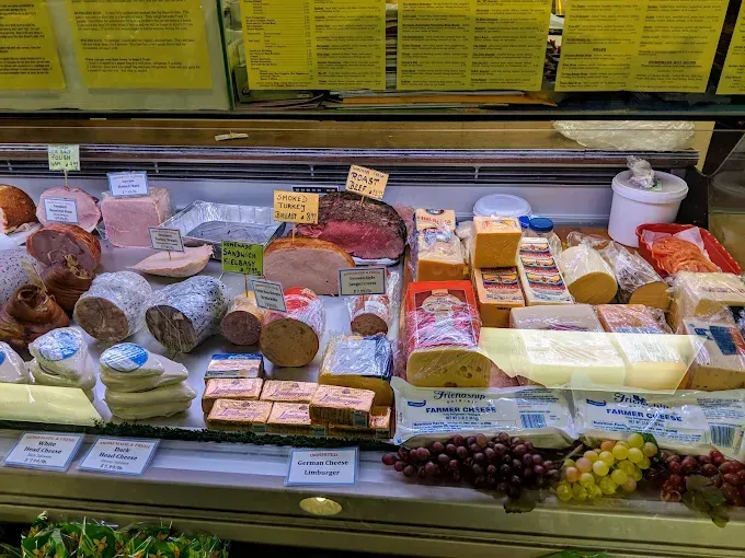 Deli case with various meats and cheeses, grapes in foreground.