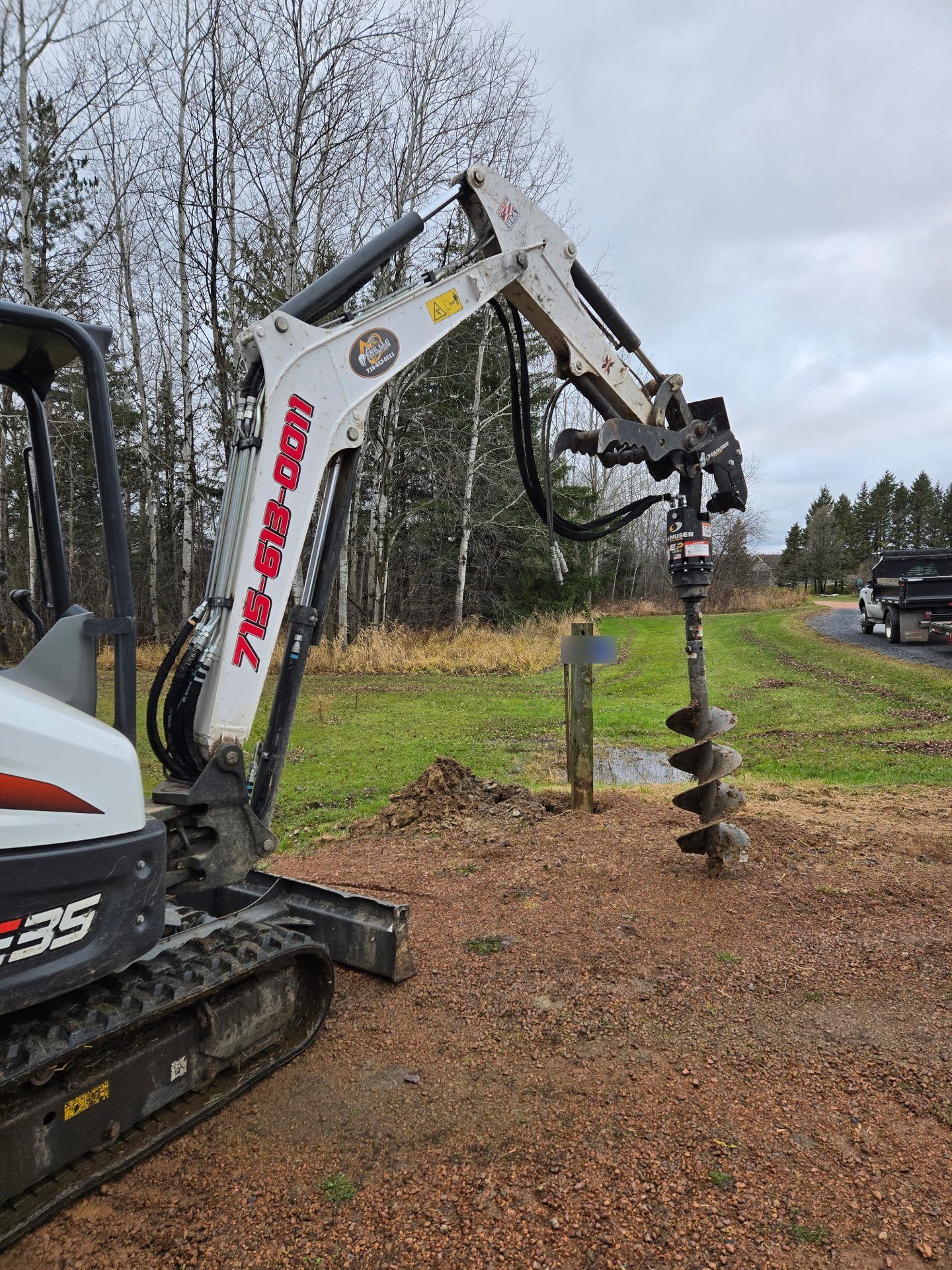 ERE mini excavator with a hydraulic auger drilling post holes for driveway entrance posts in Dorchester, WI