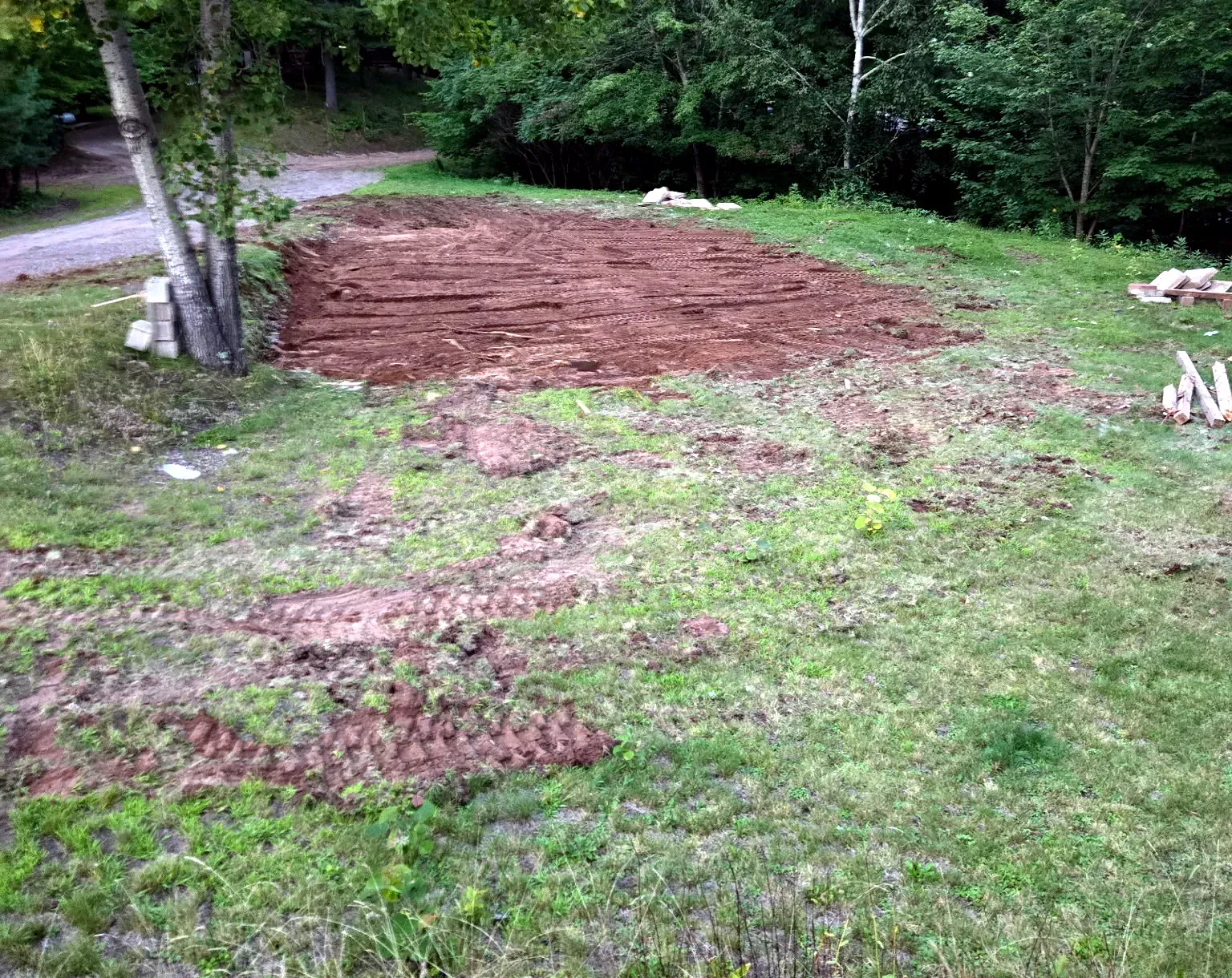 Graded soil pad left where a mobile home was demolished and removed, with the surrounding lawn cleared of debris in Phillips, WI