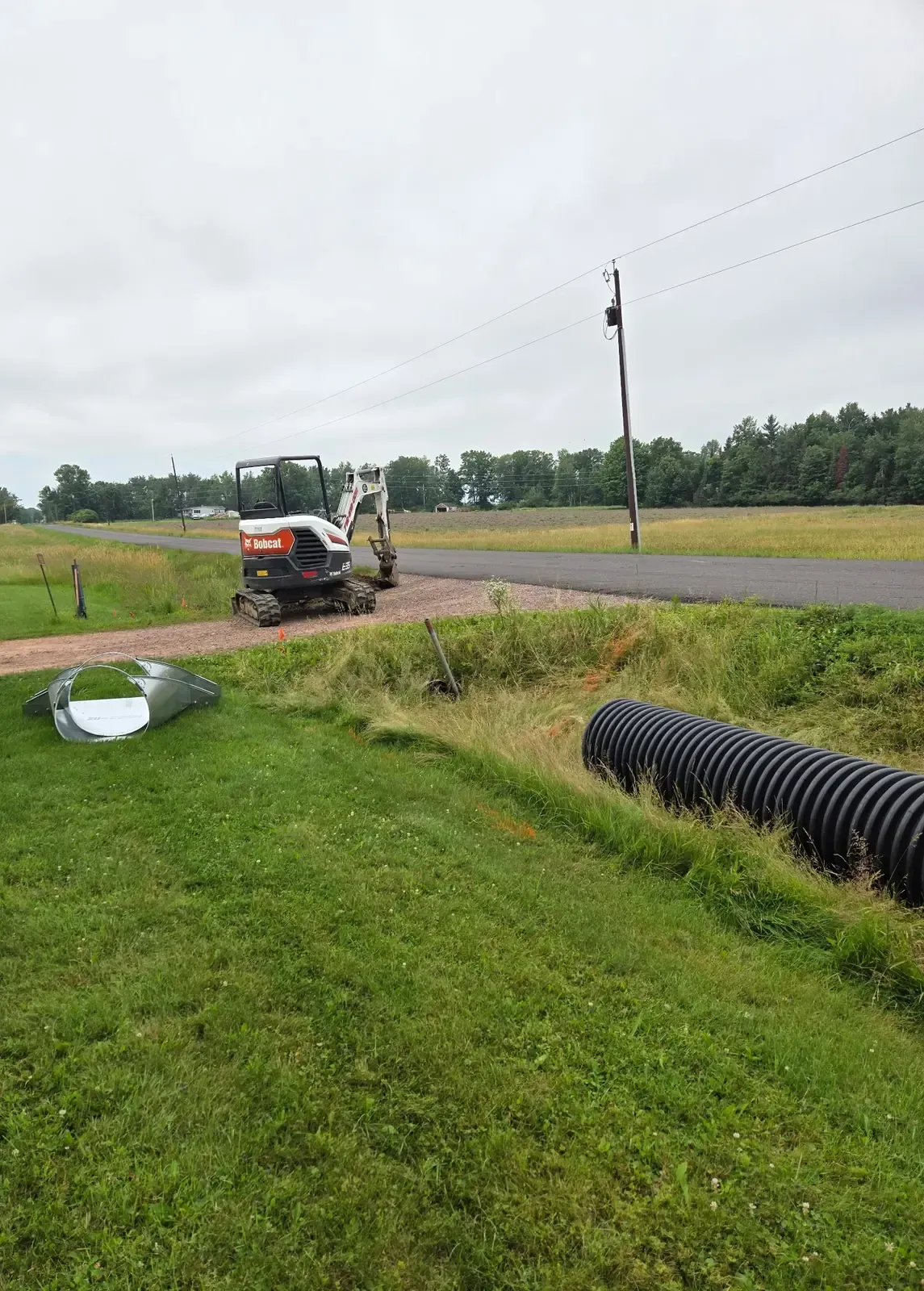 New culvert pipe and galvanized flared end section staged beside a driveway before replacement in Marshfield, WI.