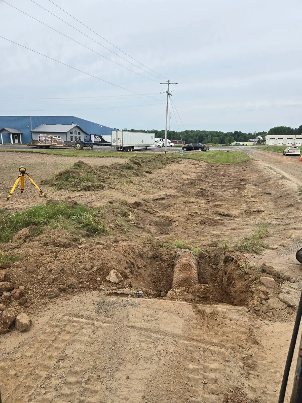 Culvert pipe set in an open trench with a laser level on a tripod nearby, Curtiss, WI – ERE Excavation