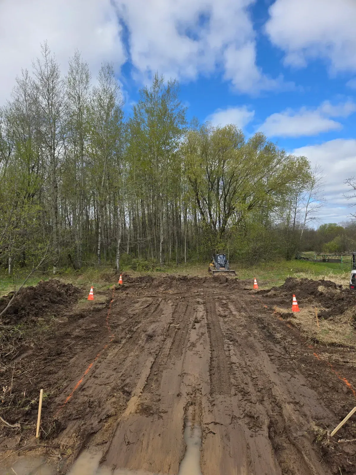 Cleared and staked ground with cones and a skid steer before a gravel parking pad in Curtiss, WI – ERE Excavation