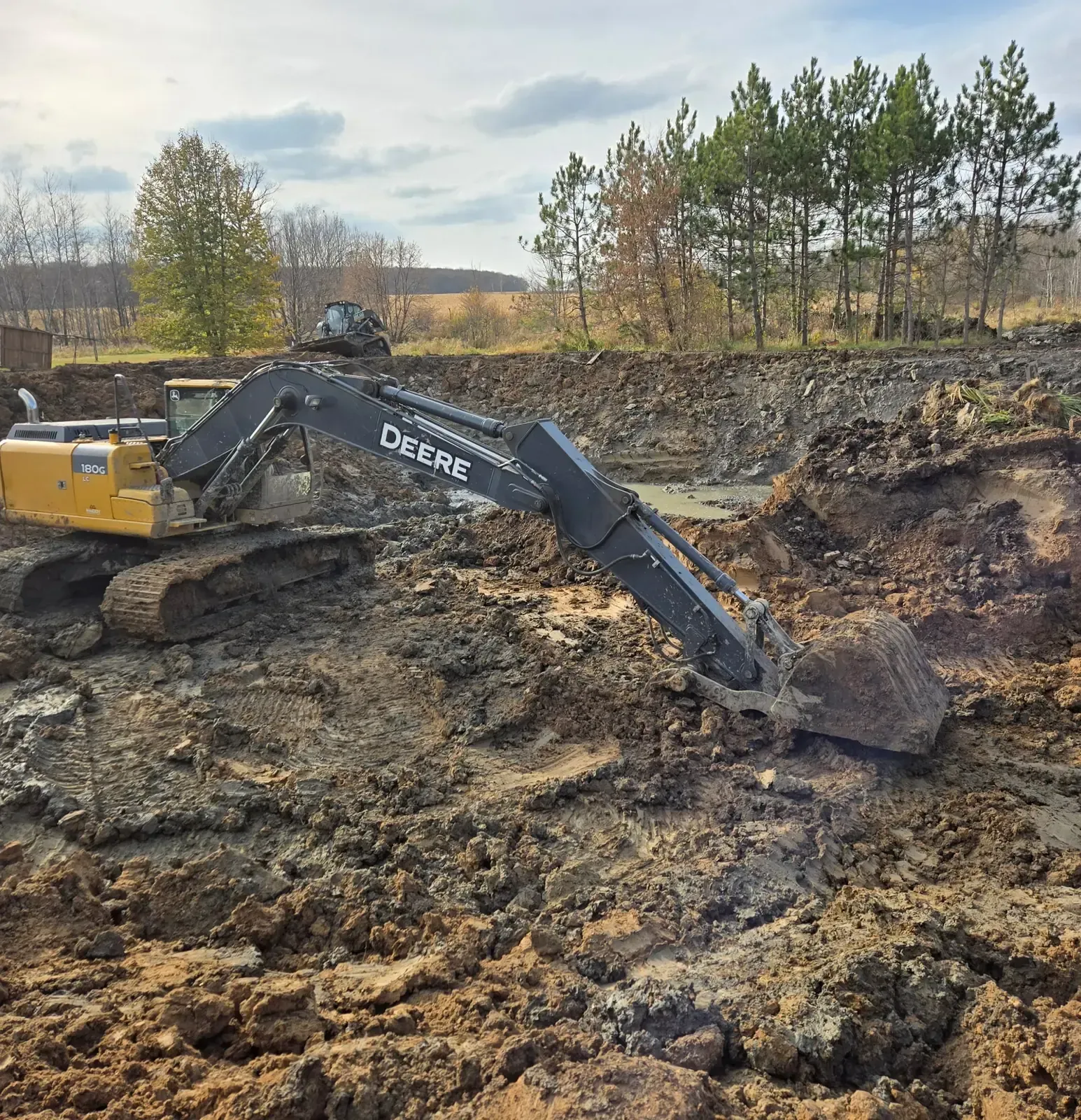 Excavator bucket digging out the muddy bottom of a pond being deepened and restored near Marshfield, WI