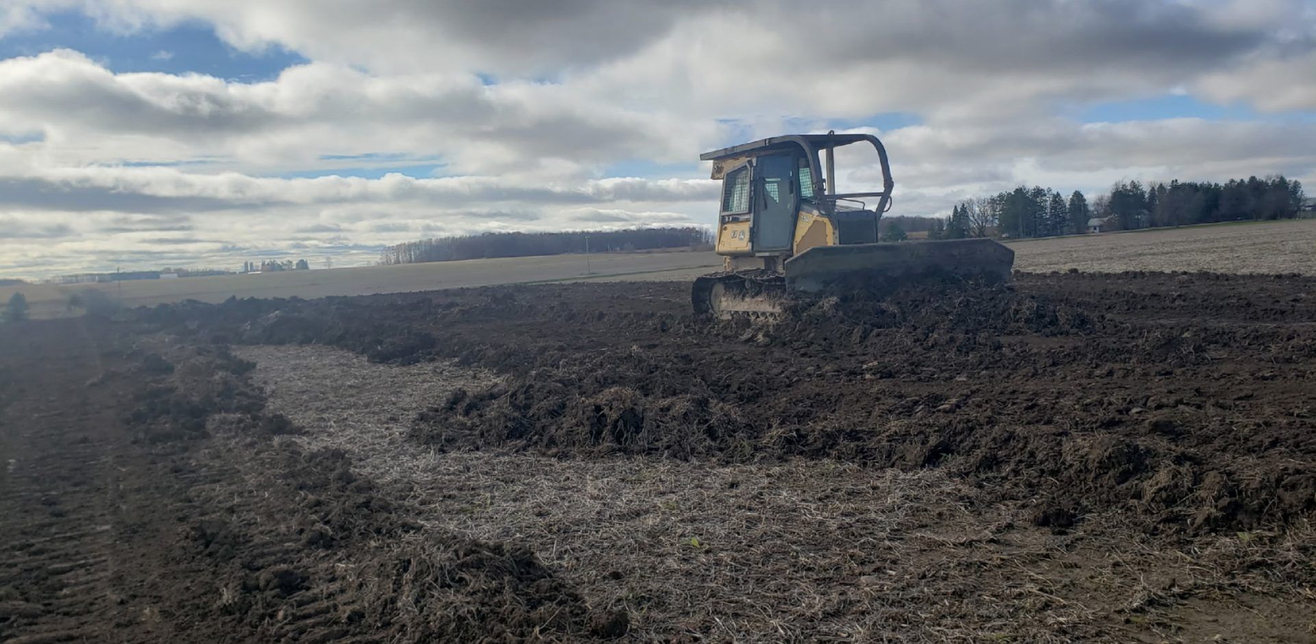 Crawler dozer leveling a reclaimed strip of farm field under fall skies in Dorchester, WI