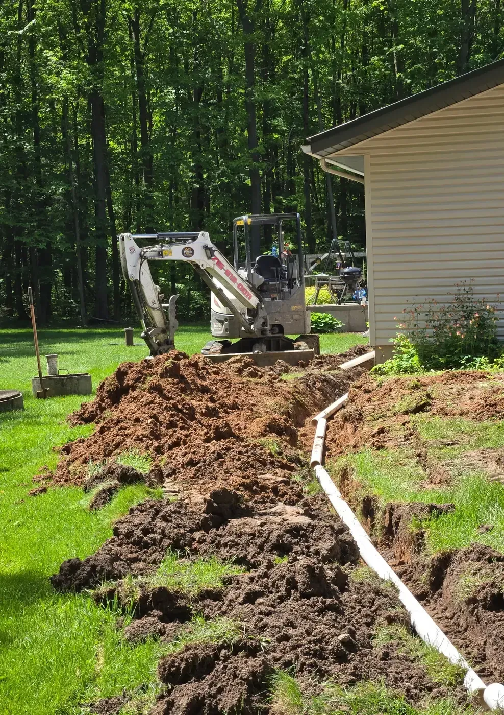 Mini excavator trenching to install a PVC drain line alongside a home in Colby, WI