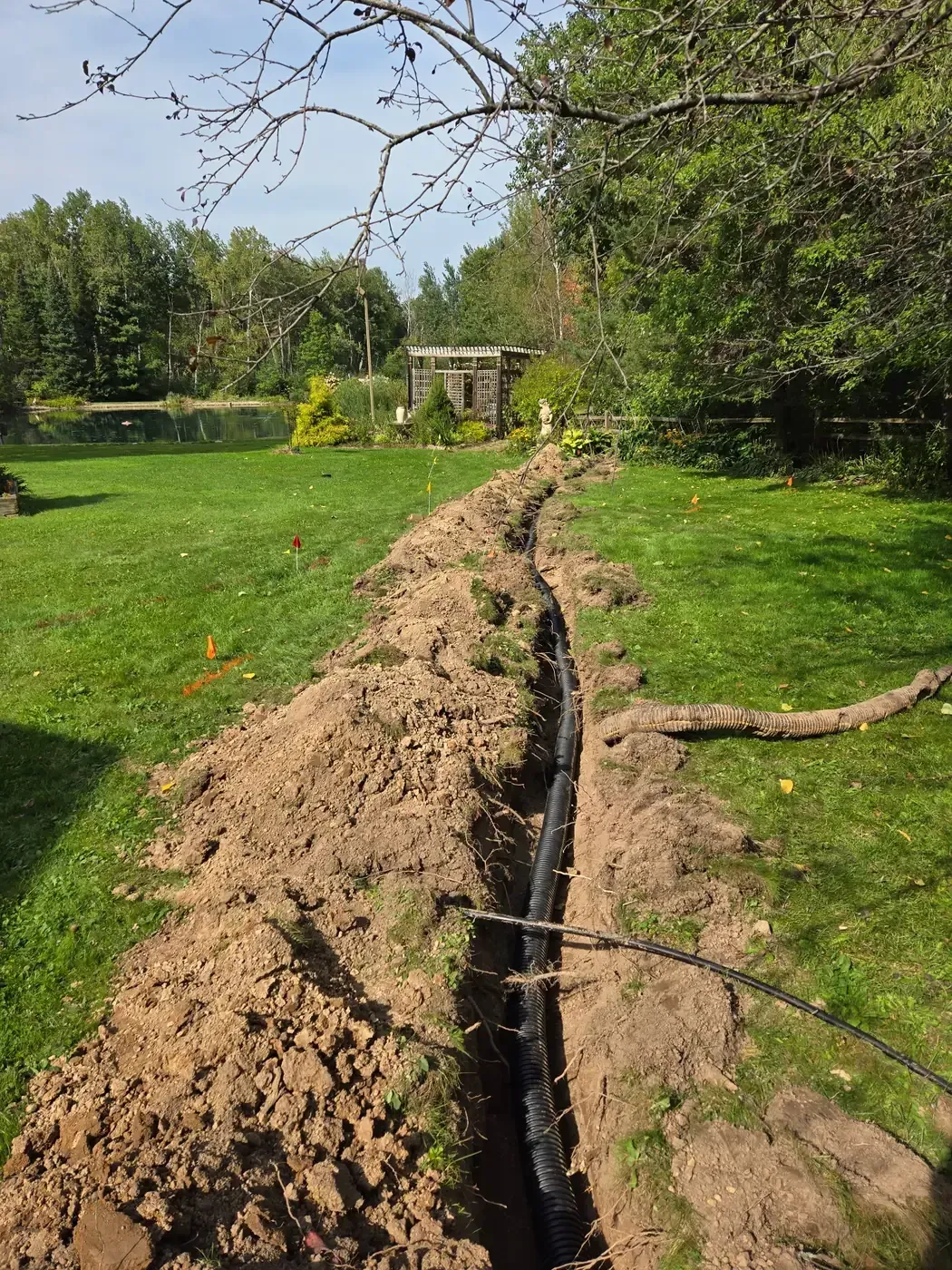 Drain tile installed in a long backyard trench with utility locate flags marked in Marshfield, WI