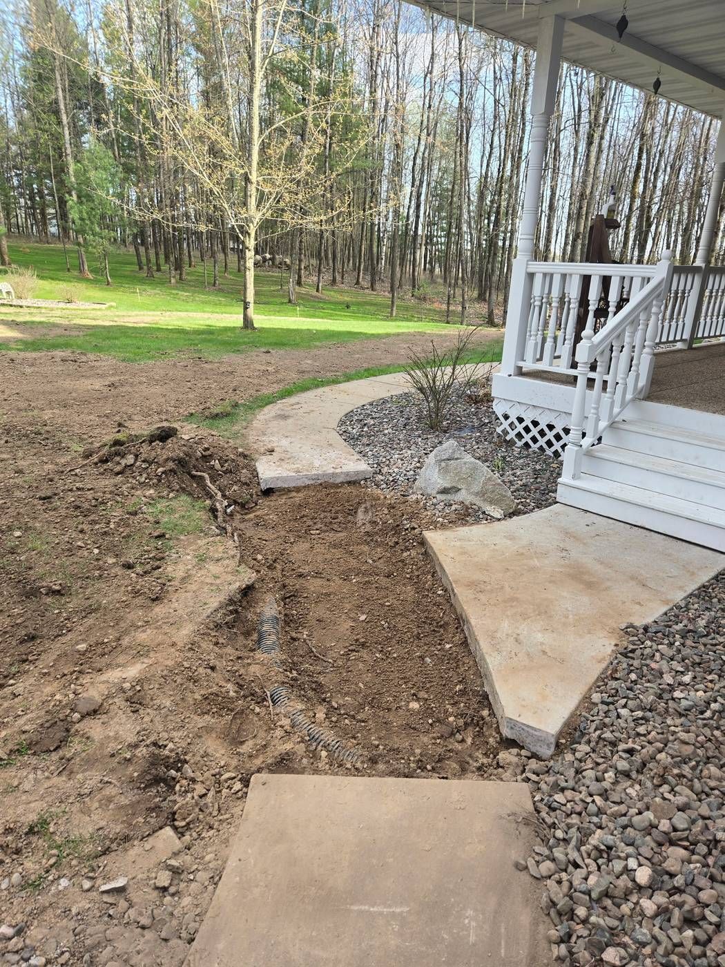 Clean saw cut through a concrete sidewalk with corrugated drain tile laid in the trench beneath it, near a home's front porch in Medford, WI