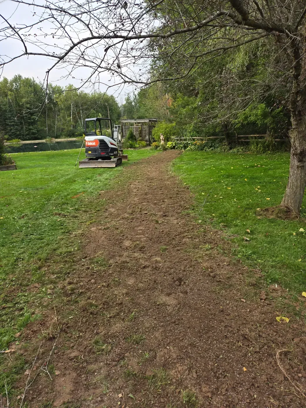 Drain tile trench backfilled and graded smooth across a backyard lawn with mini excavator on site in Marshfield, WI