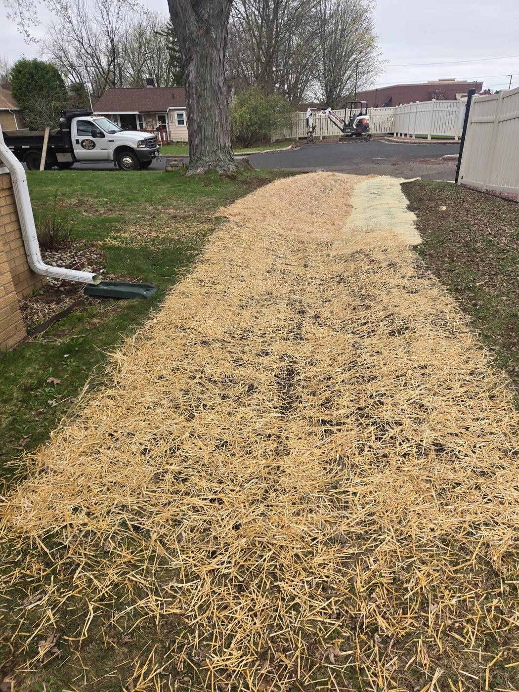 Finished drainage regrade with erosion control blanket along a home's foundation, with the ERE dump truck and mini excavator in the background in Wausau, WI
