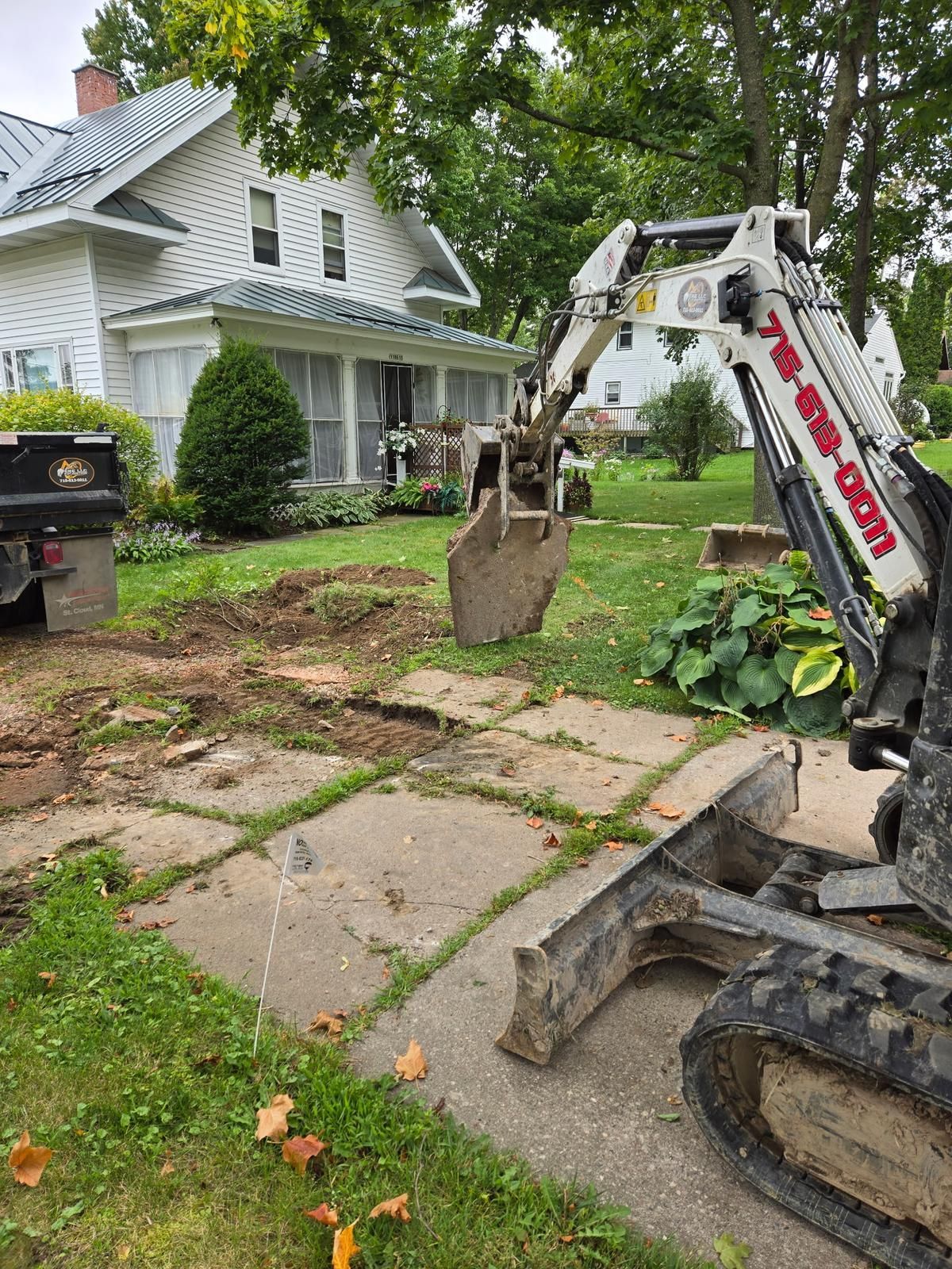 ERE mini excavator lifting a broken slab of old concrete during a residential driveway replacement in Stratford, WI