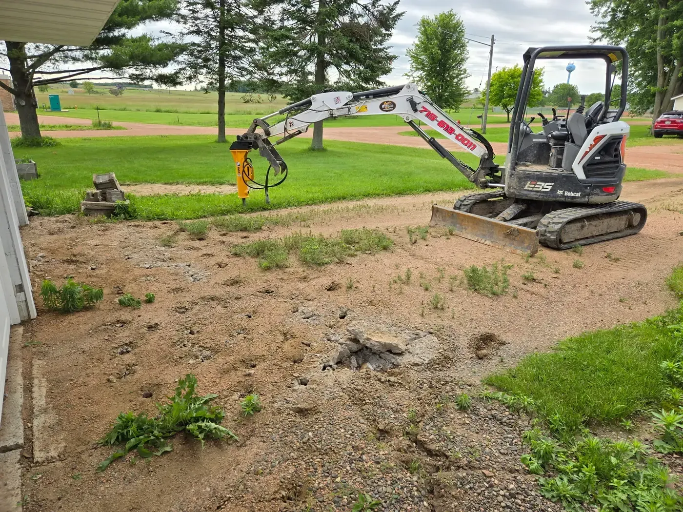 Mini excavator with a hydraulic breaker attachment tearing out an old concrete driveway in Colby, WI.