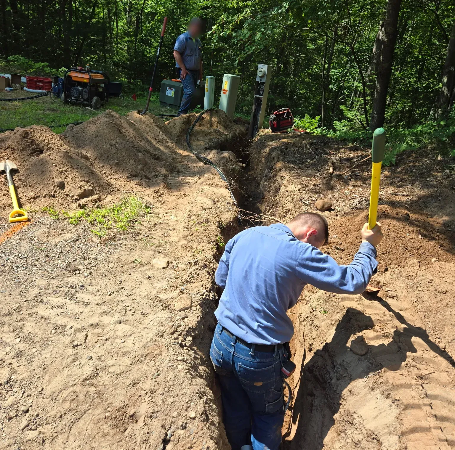 Electrician working in an open trench as buried power cable runs to the transformer, meter and utility pedestals in a wooded lot in Phillips, WI