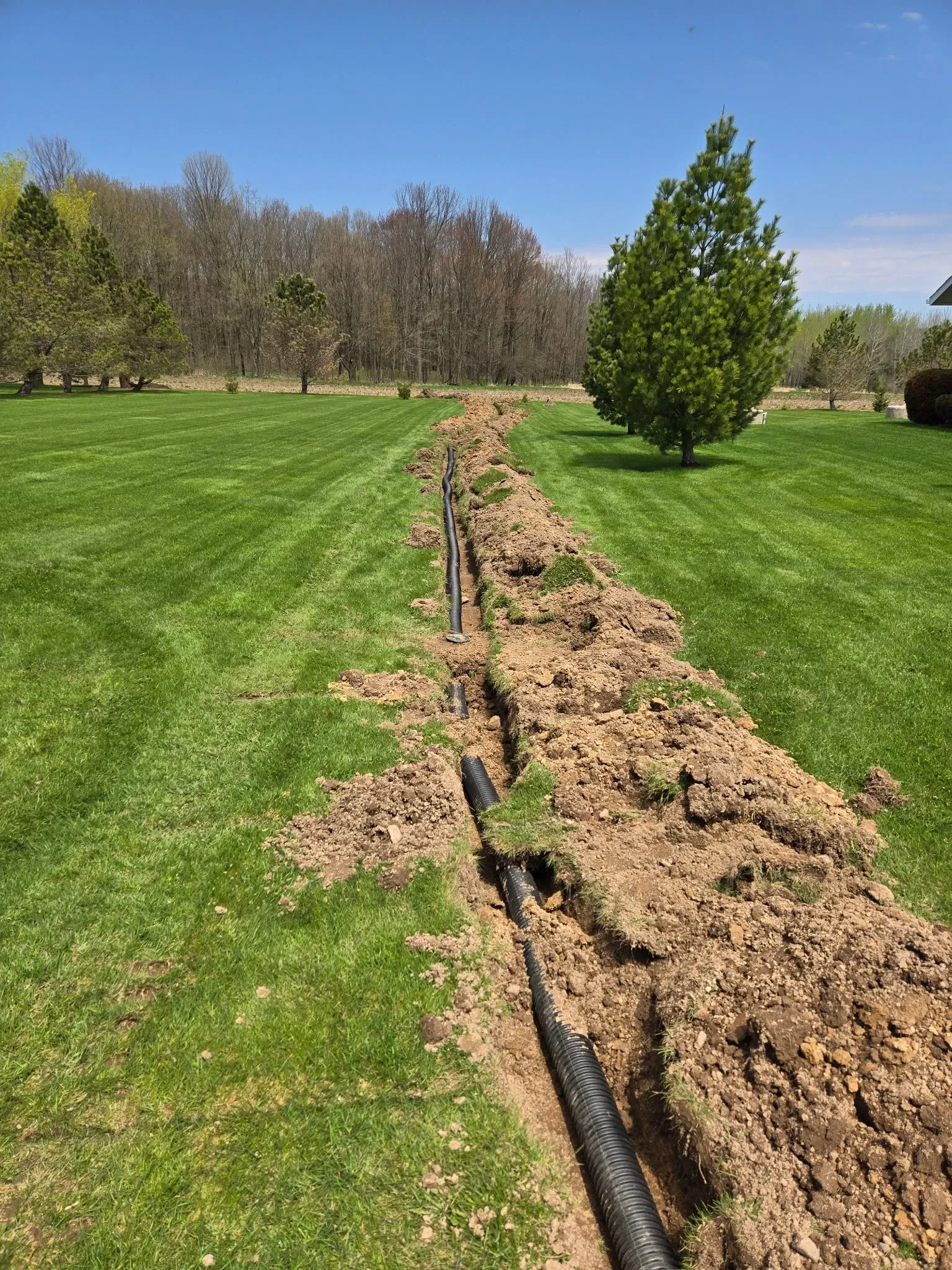 Perforated drain tile pipe being installed in a trench across a manicured lawn – ERE Excavation, Central Wisconsin