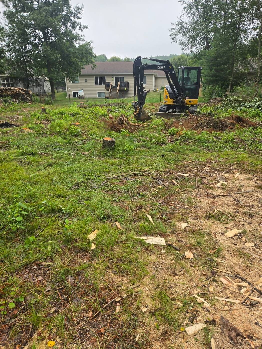 Mini excavator pulling a stump and root ball from a residential lot during land clearing in Wausau, WI
