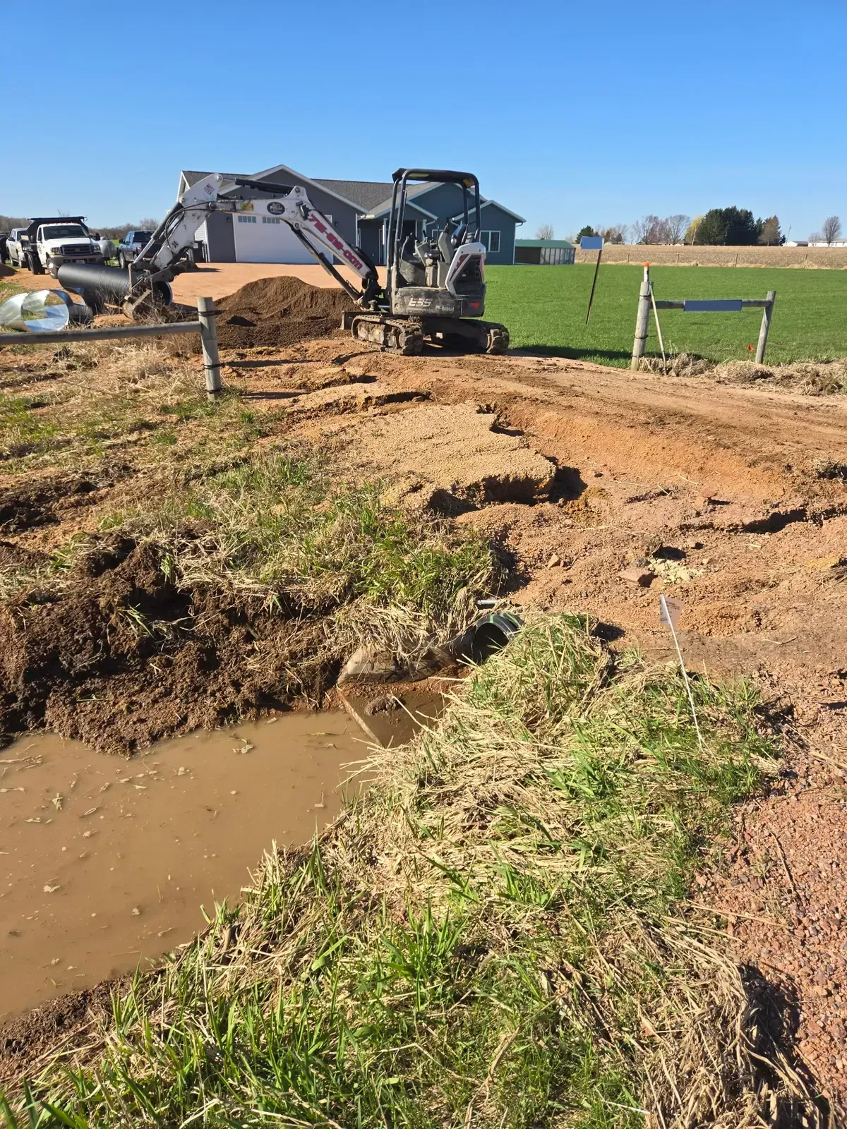 Mini excavator cutting through a driveway to replace a collapsed culvert in Marshfield, WI