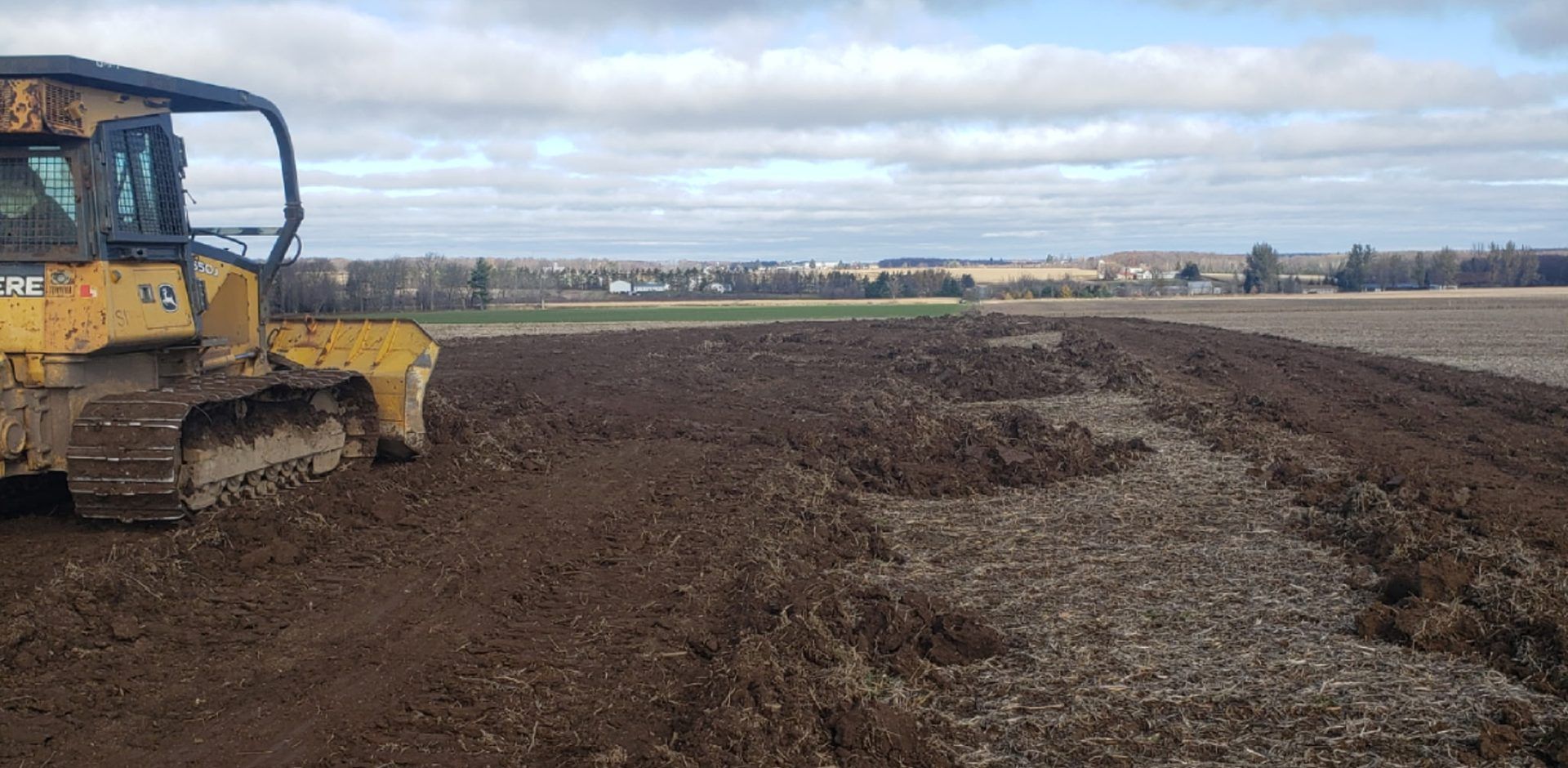 John Deere dozer pushing up old fence-line growth and spreading soil across farm field ground in Dorchester, WI