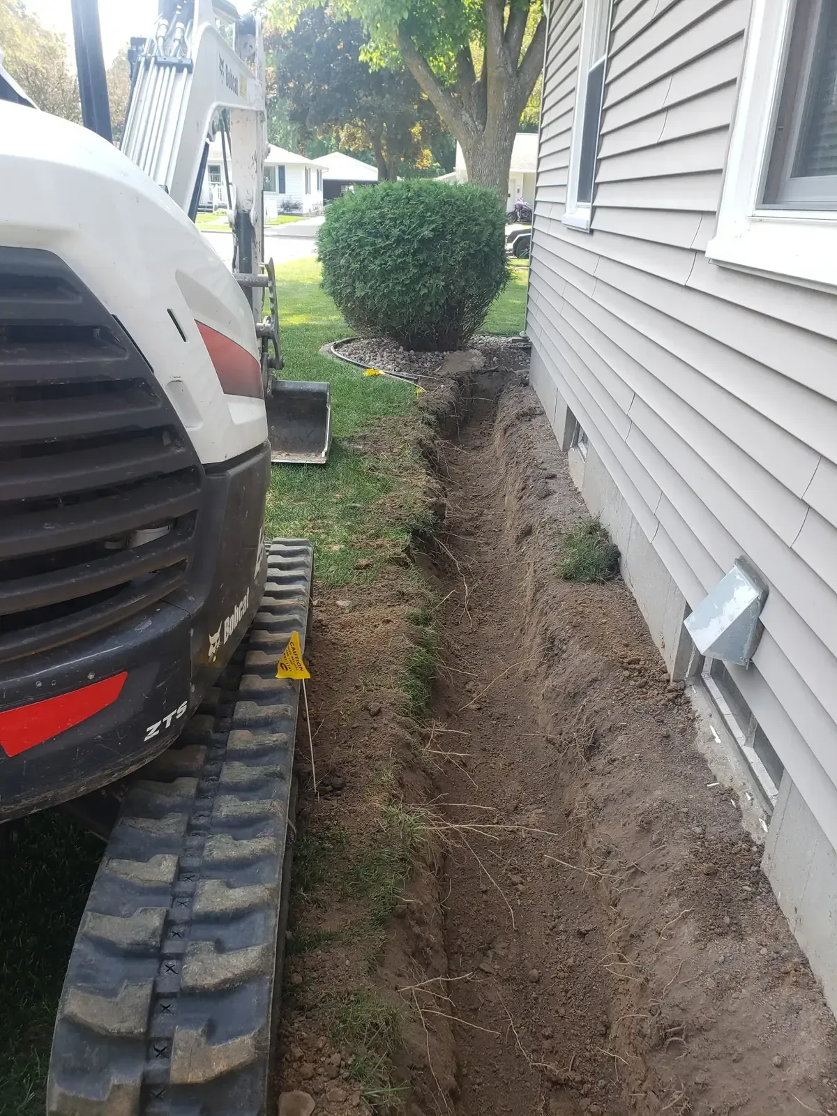 Mini excavator digging a French drain trench along a home foundation in Marshfield, WI