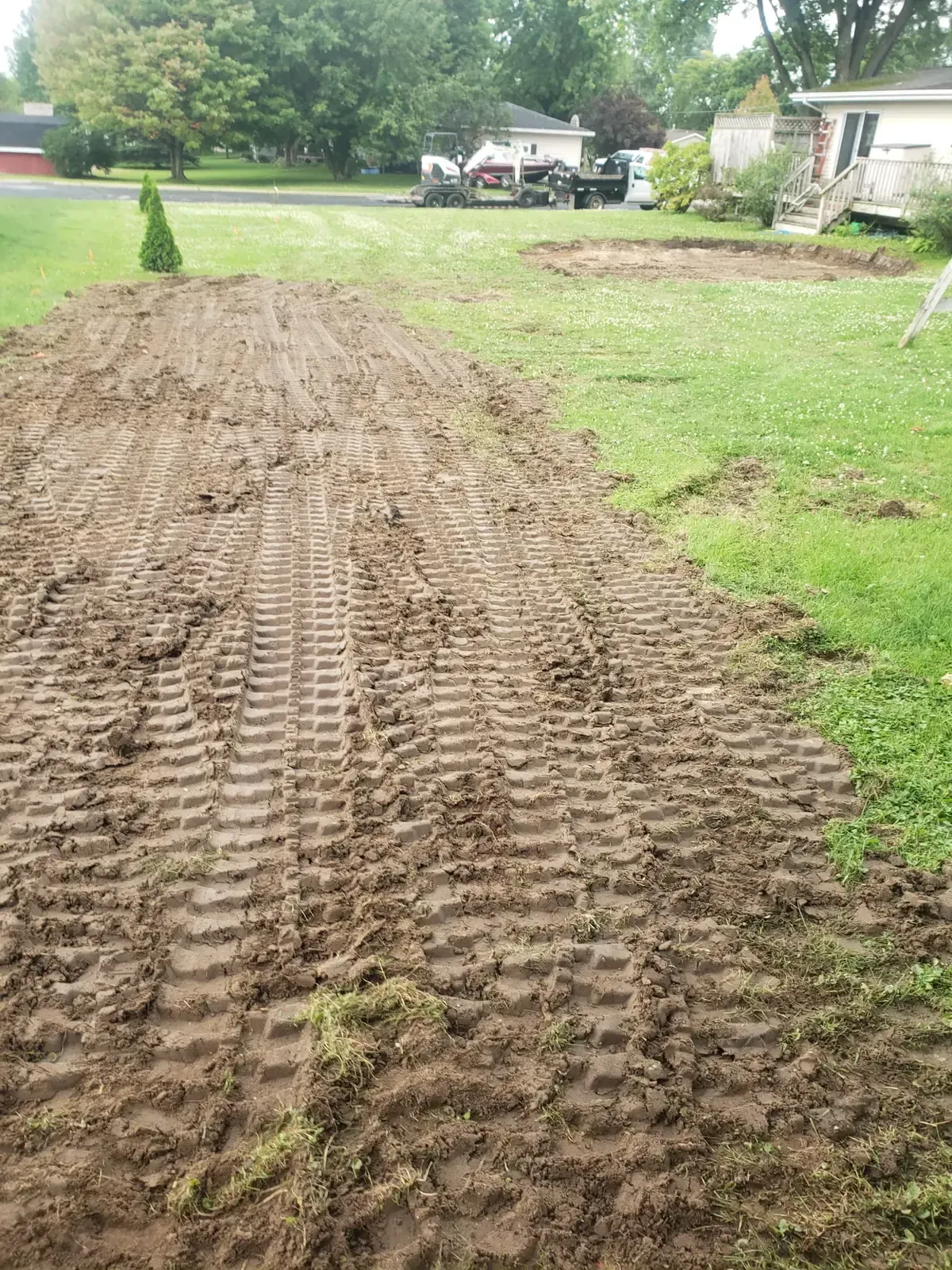 Freshly graded strip of soil where a shrub row and stumps were removed, with a cleared pool pad area in the background, in a Marshfield, WI backyard