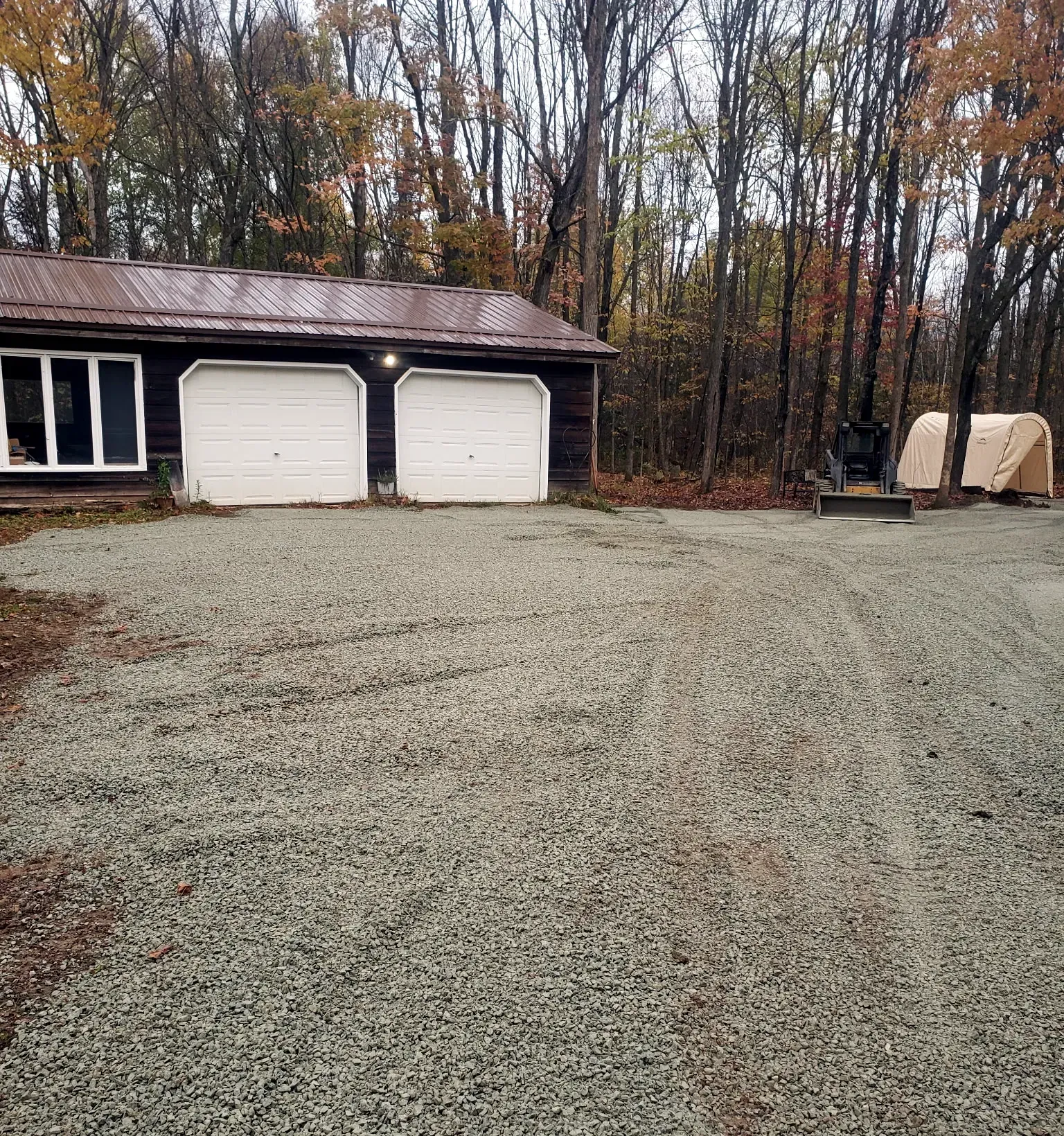 Wide crushed gravel apron spread in front of a two-stall detached garage on a wooded property in Rib Lake, WI