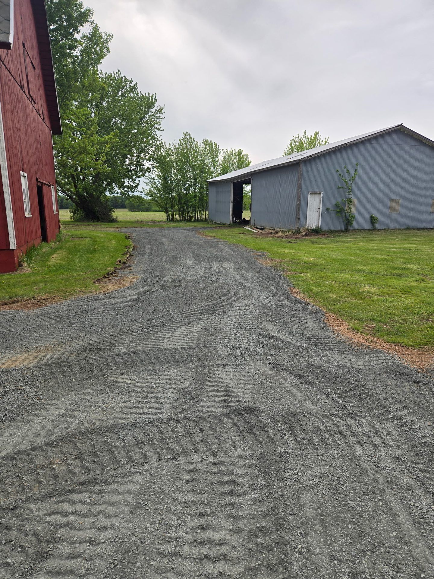 Finished farm lane resurfaced with new crushed gravel between a red barn and machine shed in Dorchester, WI