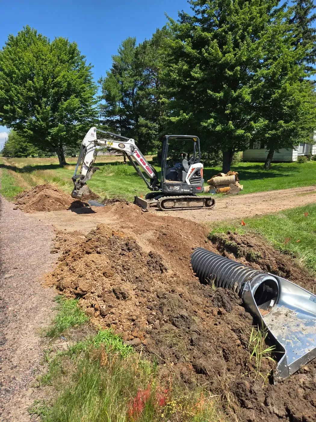Mini excavator installing a new driveway culvert with flared end section, old rusted culverts removed, in Marshfield, WI.
