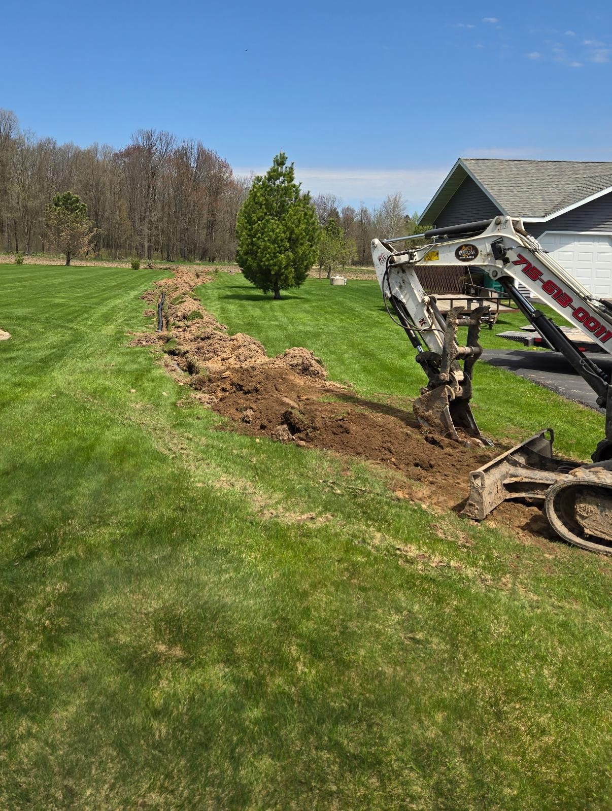 Long drain tile trench across a rural Medford, WI yard with ERE excavator in foreground