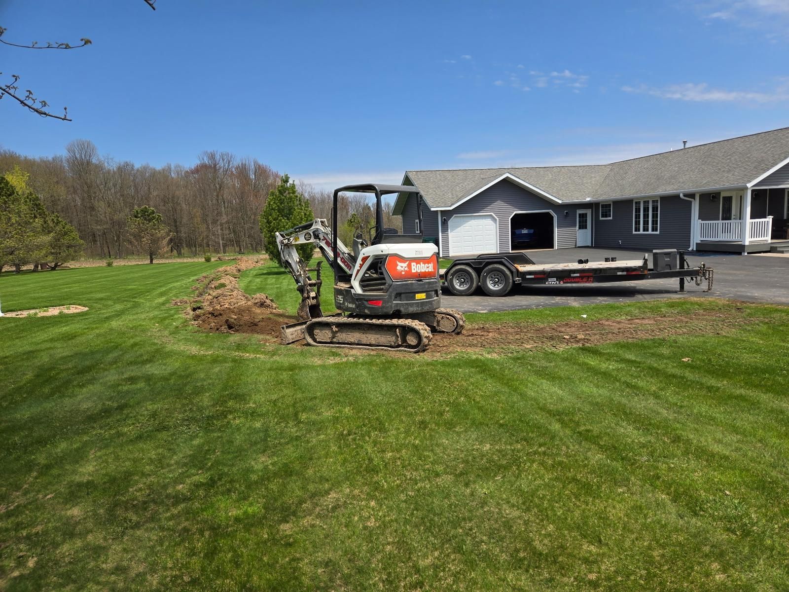 Mini excavator digging a drain tile trench beside a home in Medford, WI