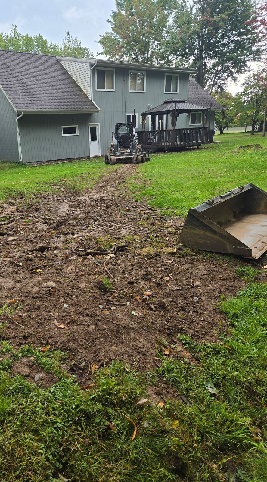 Skid steer with landscape rake regrading a backyard after utility line burial in Medford, WI