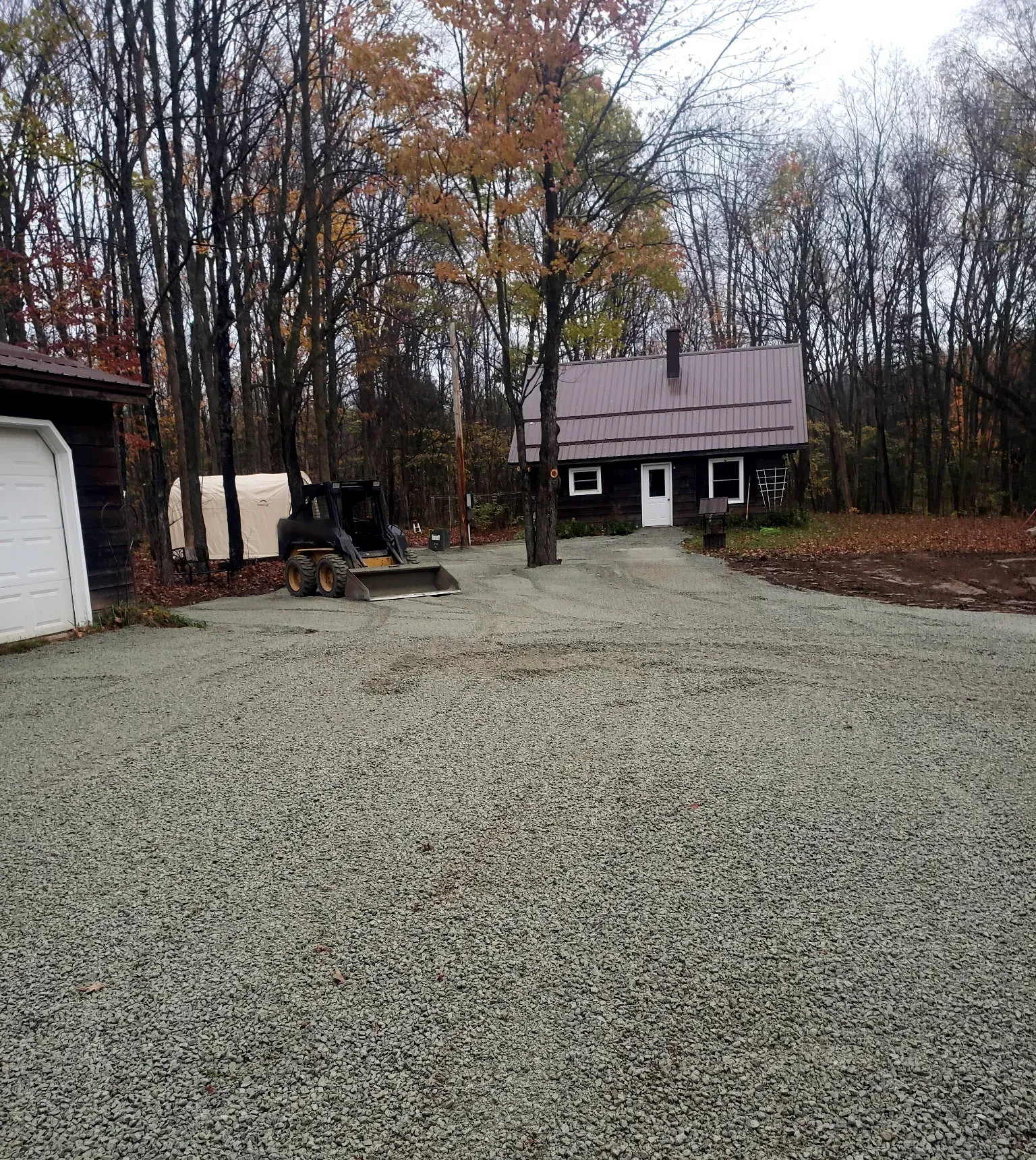Newly installed crushed gravel driveway and parking area leading to a metal-roofed home in the woods in Rib Lake, WI