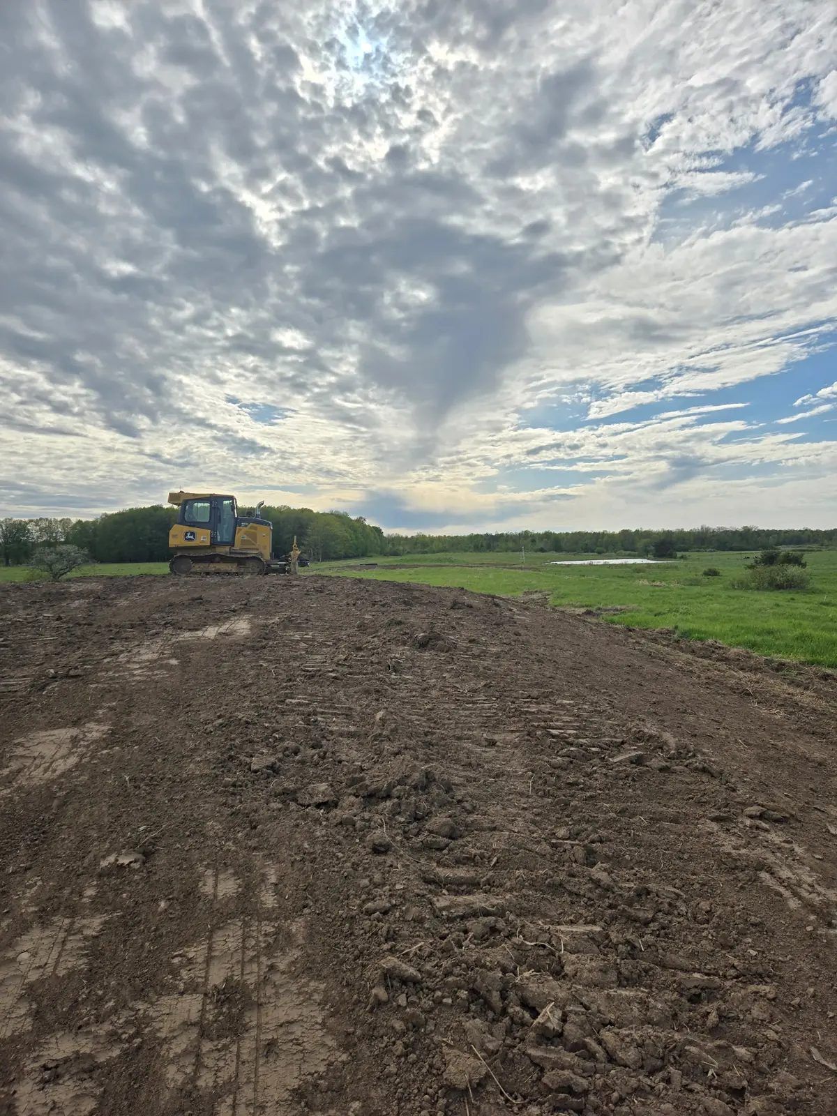 Bulldozer shaping a long stretch of newly graded earth beside green pasture on a conservation project near Marshfield, WI