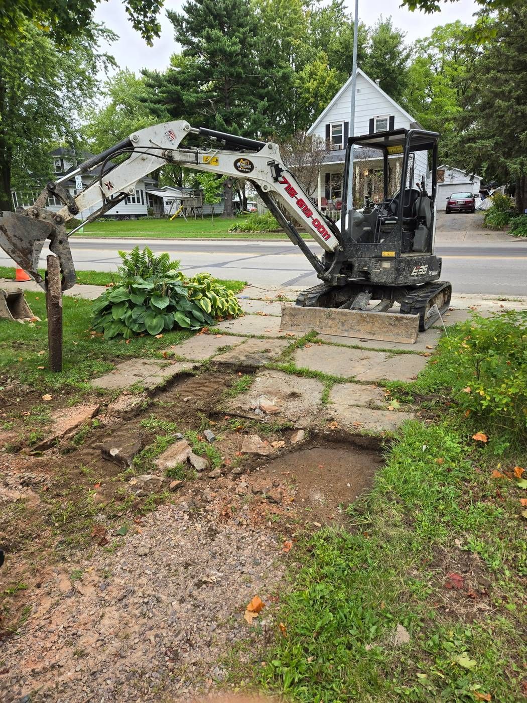 Cracked old concrete driveway partially torn out and excavated next to an ERE mini excavator in Stratford, WI