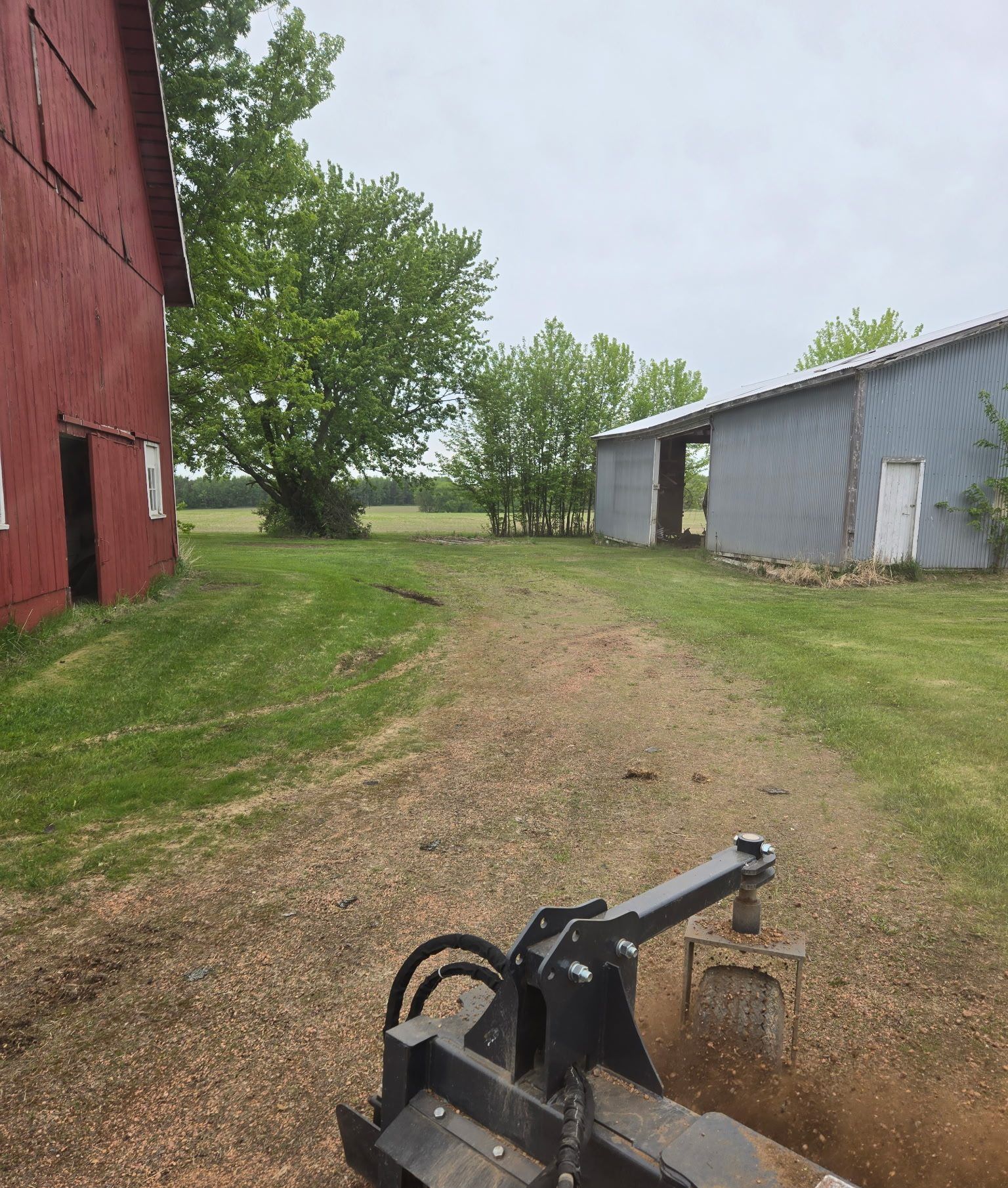 Power rake attachment reconditioning a worn, grassed-over farm lane between barns in Dorchester, WI