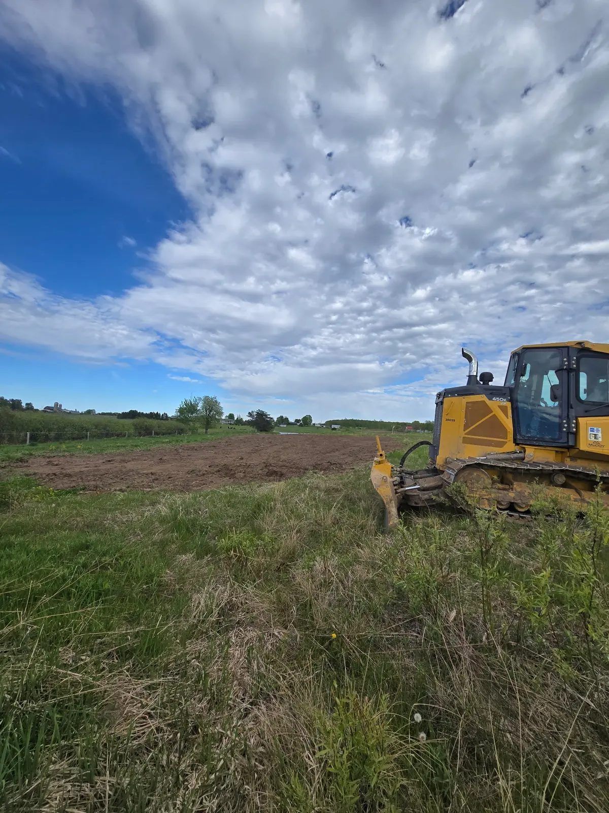 Bulldozer beside a regraded section of pasture with farm buildings and silos on the horizon near Marshfield, WI