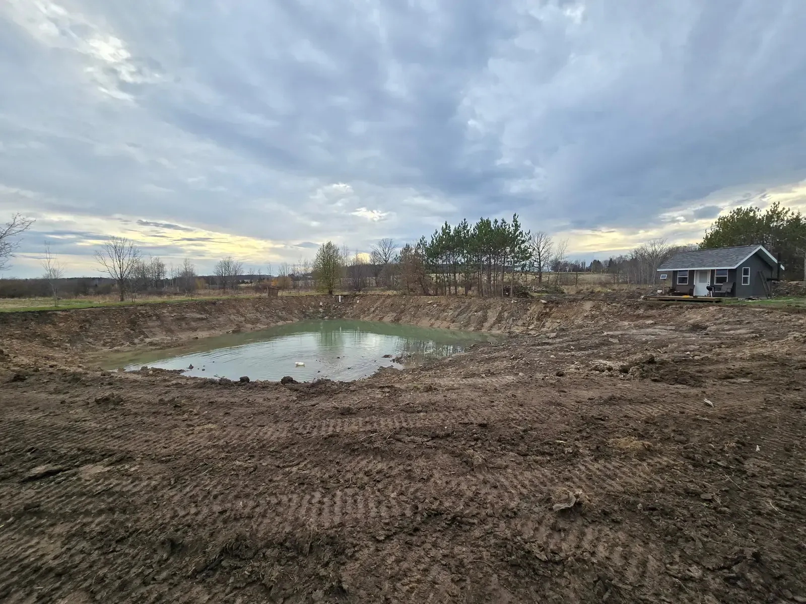 Wide view of a restored pond refilling with clear water inside newly dug and sloped banks on a rural property near Marshfield, WI