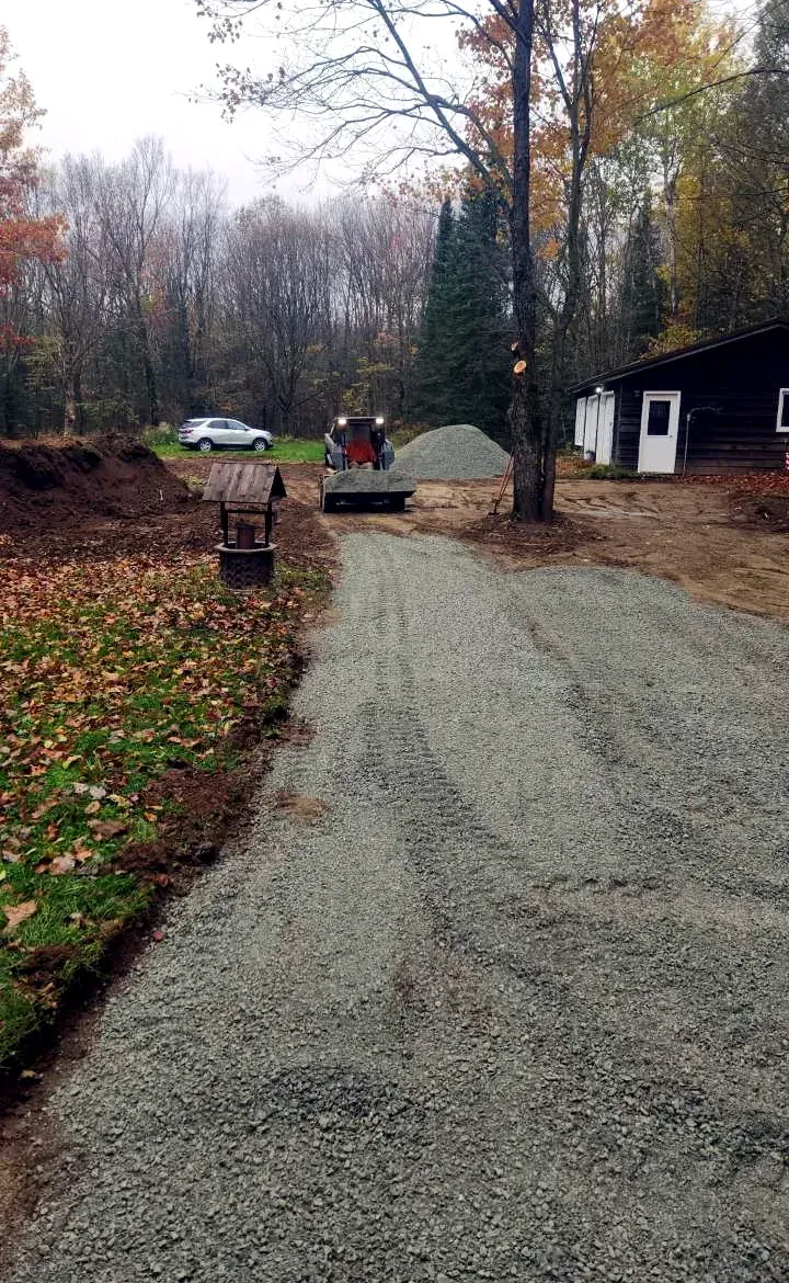 Skid steer hauling a bucket of crushed gravel to build a new driveway through a wooded lot in Rib Lake, WI