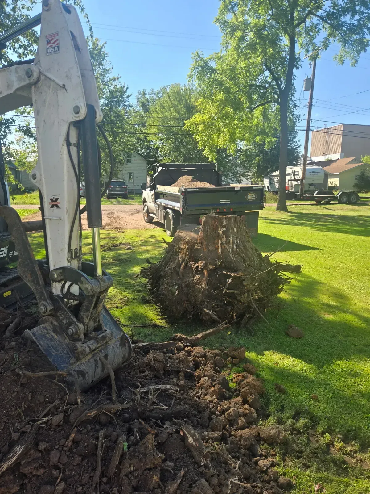 Large tree stump and root ball pulled from a residential yard with a mini excavator and fill dirt ready in the dump truck in Abbotsford, WI