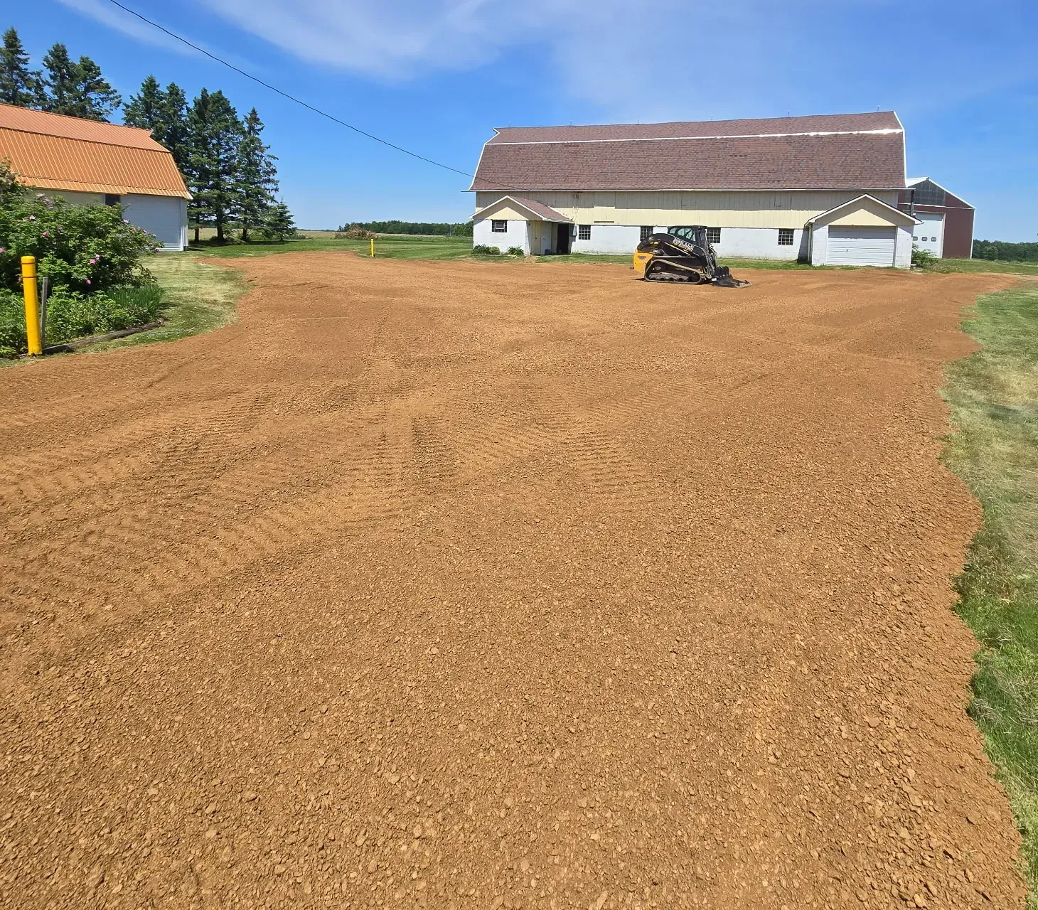 Wide barnyard driveway freshly top dressed with crushed red gravel, with an ERE track loader parked by a gambrel-roof barn in Spencer, WI