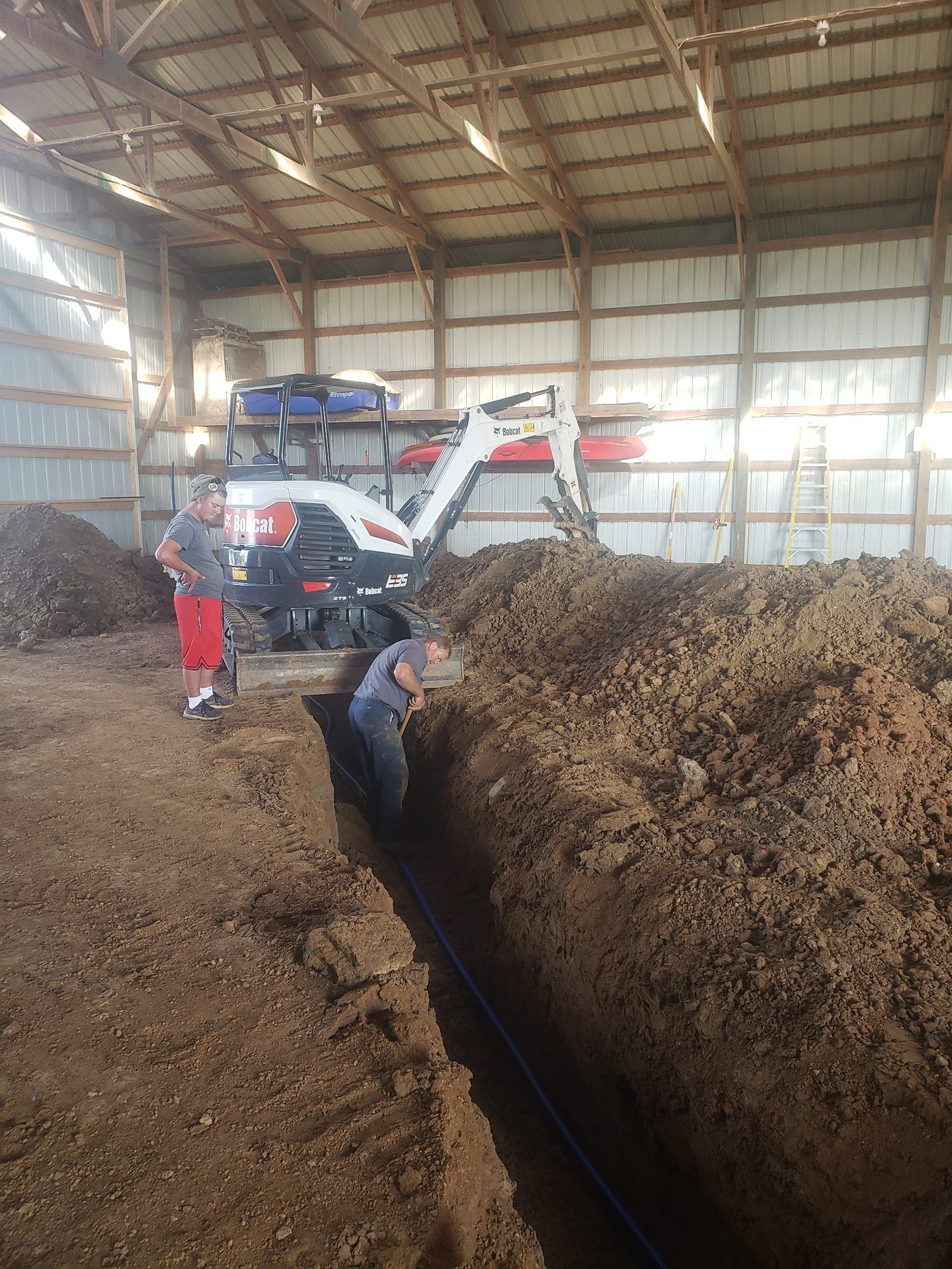 Mini excavator trenching through a pole shed floor while crew lay a new PEX water line in Dorchester, WI