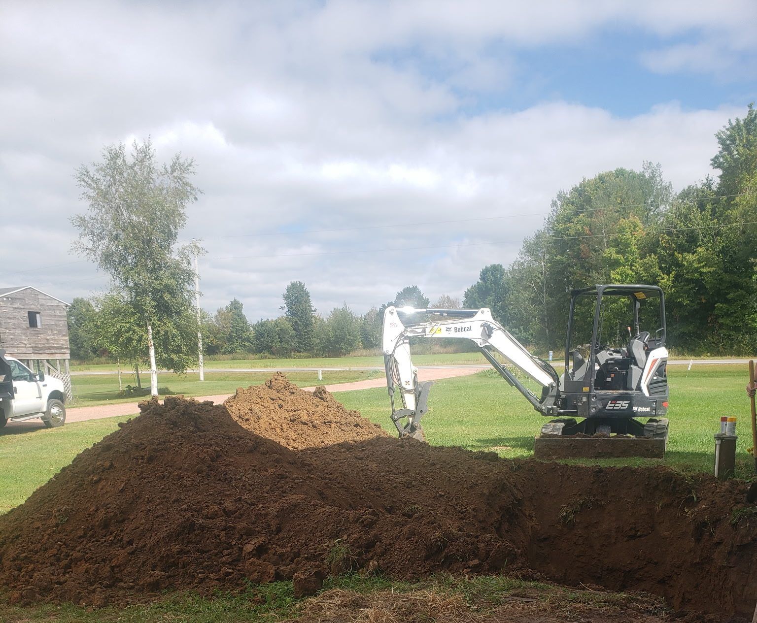 Bobcat mini excavator trenching across a yard from the well to a pole shed for a new water line in Dorchester, WI