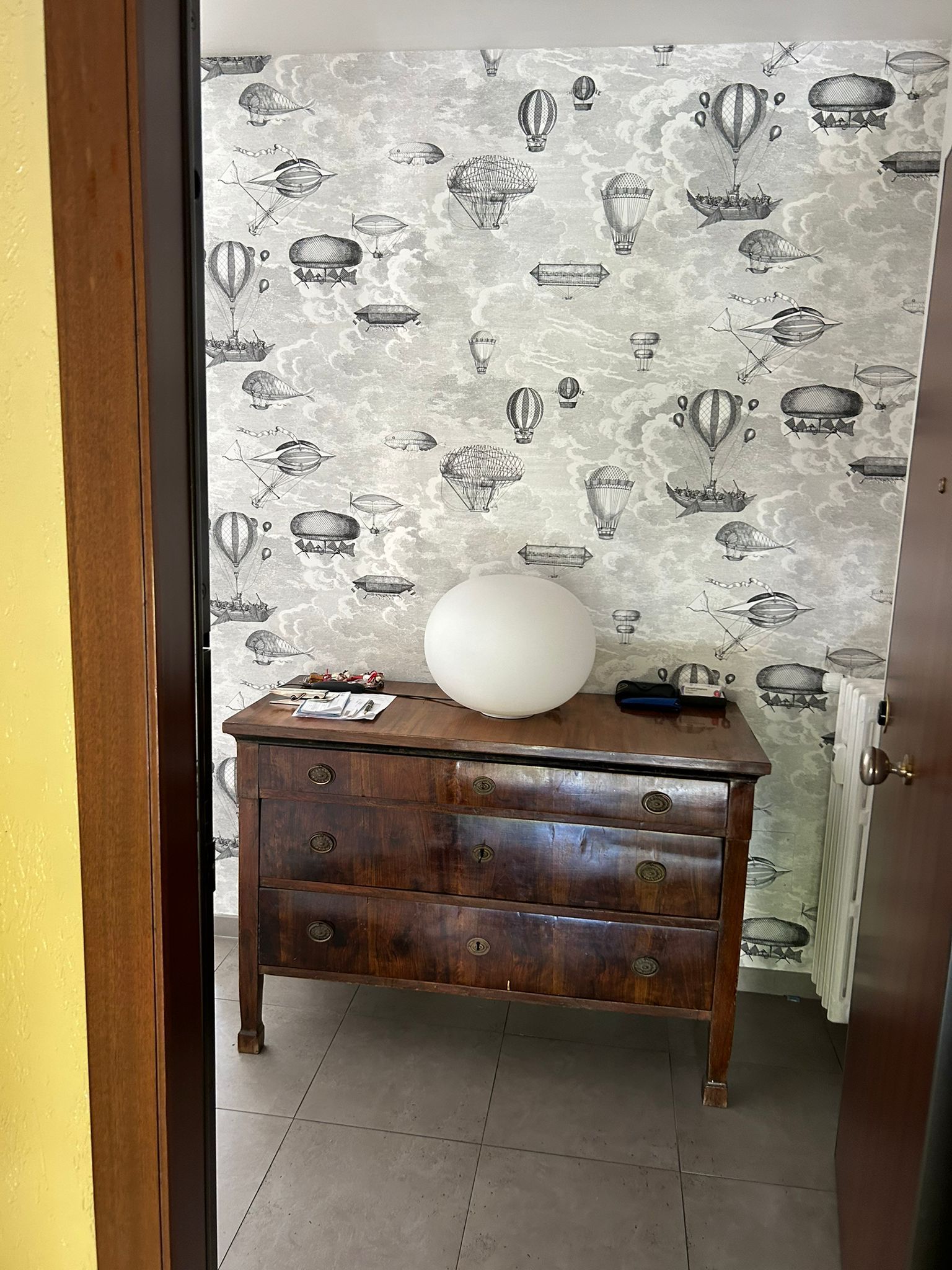 Una stanzetta con carta da parati a motivi di pesci, una cassettiera in legno e un grande palloncino bianco sopra.