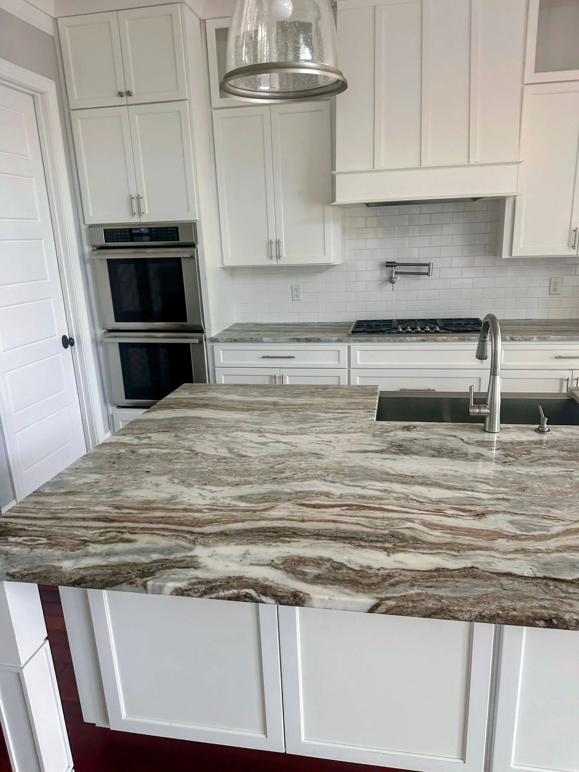 Modern white kitchen with granite island, built-in ovens, and stainless range hood