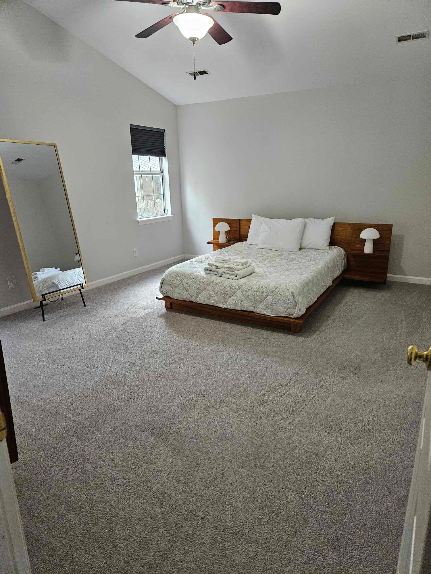 Bedroom with bed, mirror, window, and two lamps. Gray walls and carpet.